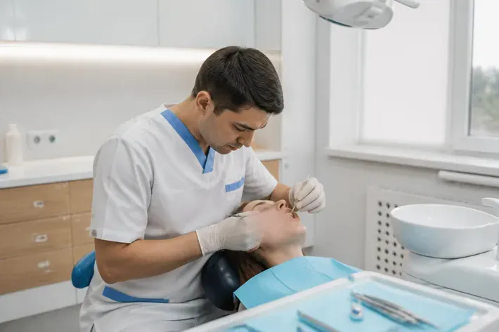Орындық жанындағы қабылдау: жұмыс үстіндегі дәрігер, ассистенттің иығынан түсірілген сурет — «Тілік жасап күрделі жұлу» бөліміне иллюстрация