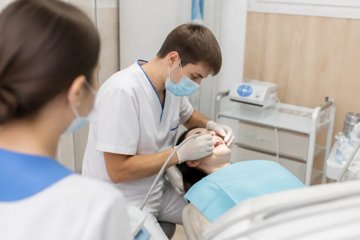 Chairside appointment: dentist at work, over-the-shoulder view of the assistant — illustration for the section "Indications, limitations, and follow-up"