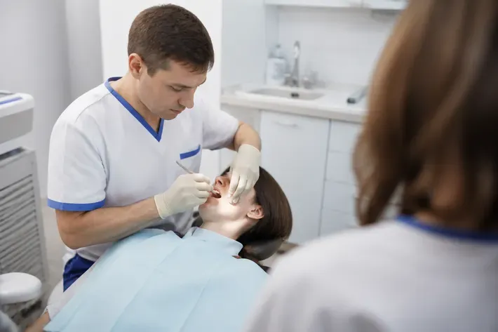 Орындықтағы қабылдау: жұмыс үстіндегі дәрігер, көмекшінің иығынан түсірілген сурет — «Самай-жақ буыны ауруларындағы операциялар» бөліміне иллюстрация