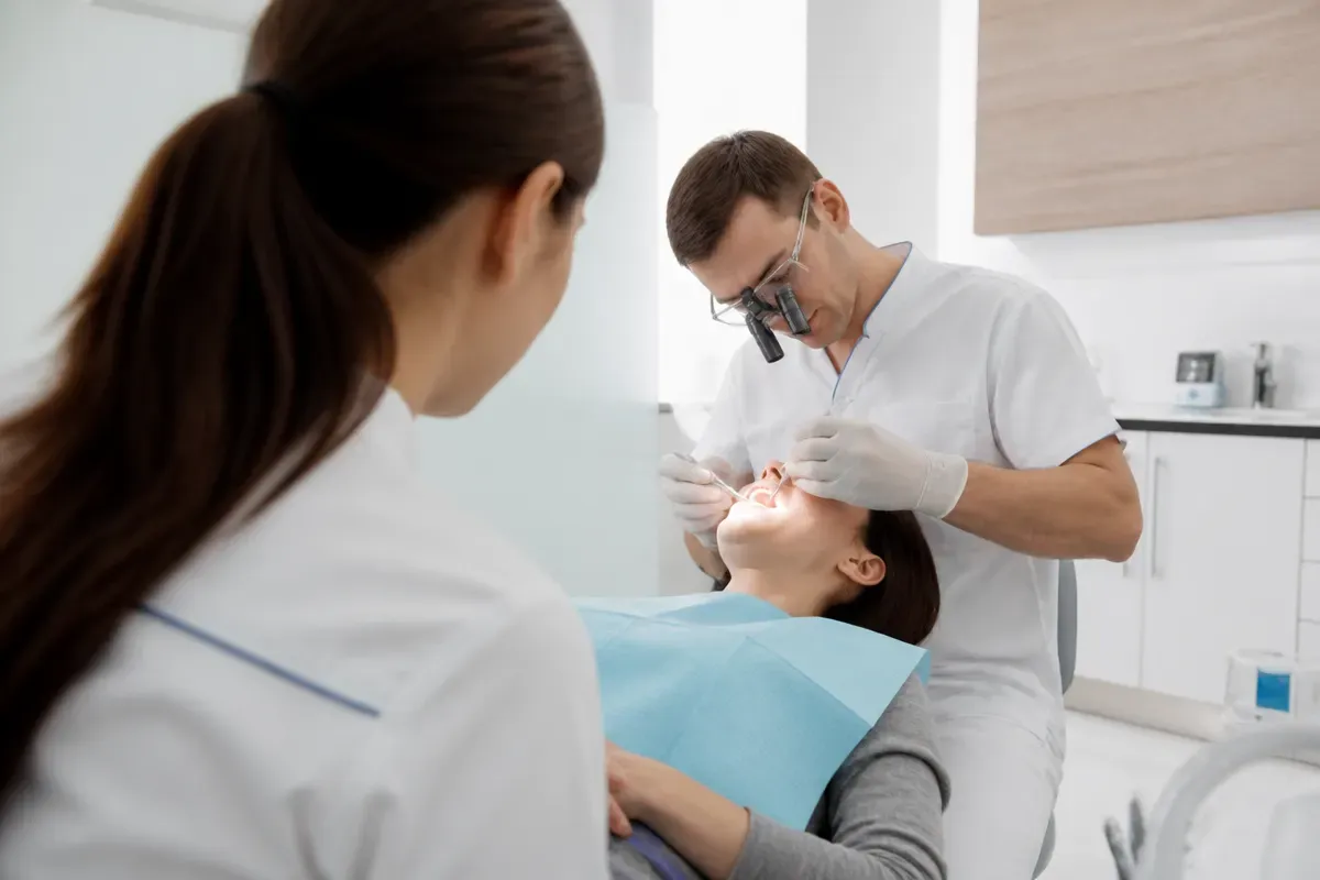 Chairside appointment: dentist at work, over-the-shoulder shot of the assistant — illustration for the section "Zirconia crowns with veneering"