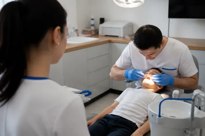 Chairside appointment: dentist at work, over-the-shoulder shot of the assistant — illustration for the section "Pediatric cosmetic dentistry: which procedures are possible"