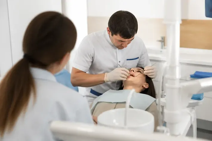 Chairside appointment: dentist at work, over-the-shoulder shot past the assistant — illustration for the section "What types of implants exist"