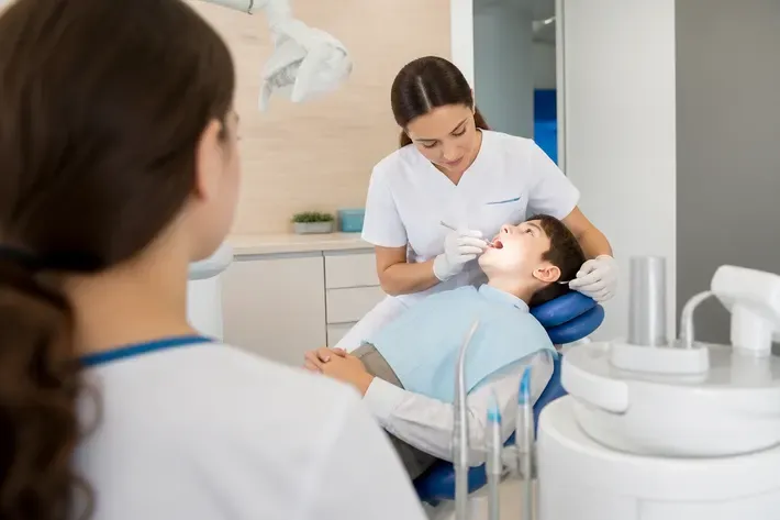 Chairside visit: dentist at work, shot over the assistant's shoulder — illustration for the "Trainers" section