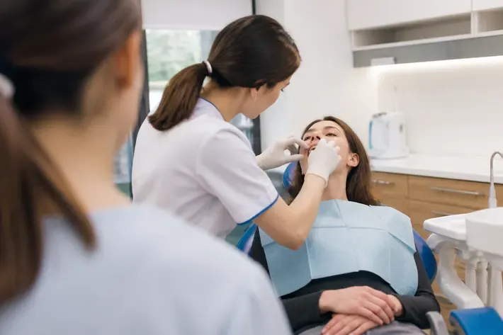 Chairside appointment: dentist at work, over-the-shoulder shot past the assistant — illustration for the "Clear Aligners" section