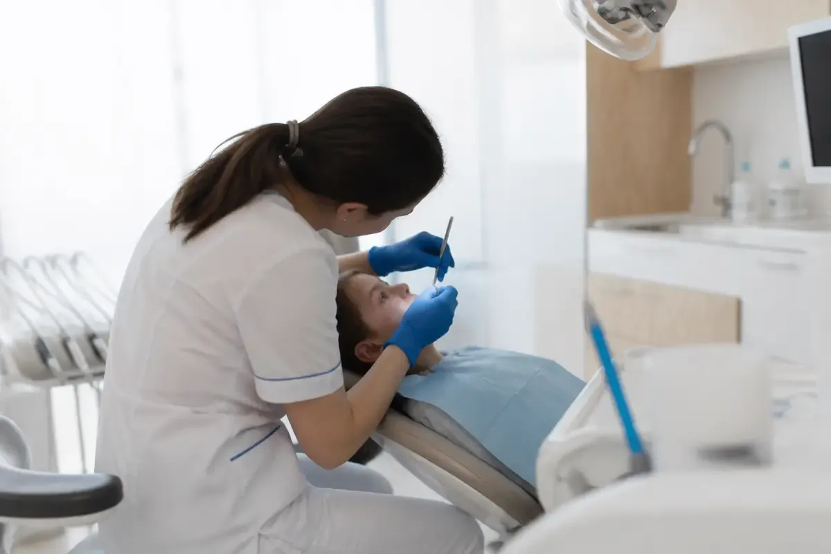 Chairside appointment: dentist at work, over-the-shoulder view of the assistant — illustration for the section "Monitoring and possible complications"
