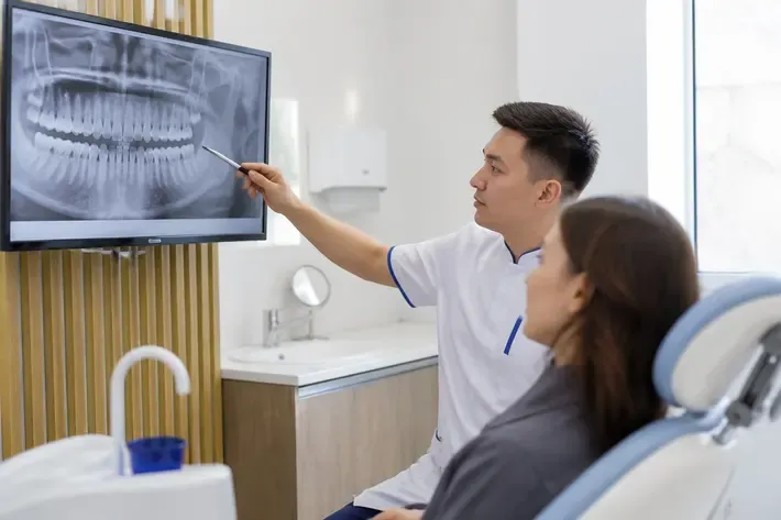 The doctor shows the patient an image on the screen and explains the treatment plan — an illustration for the section "Laser gum correction: which aesthetic issues it addresses"