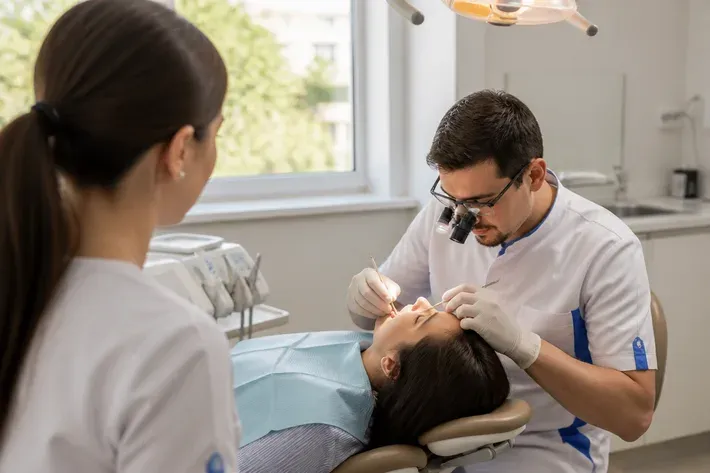 Chairside appointment: dentist at work, over-the-shoulder shot of the assistant — illustration for the section "What causes a dental cyst"