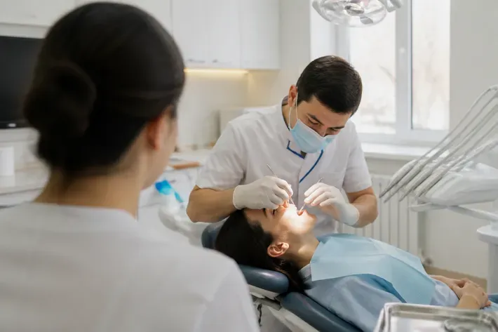 Chairside appointment: dentist at work, shot over the assistant's shoulder — illustration for the section "What treatments for periodontal disease exist and how do they differ"