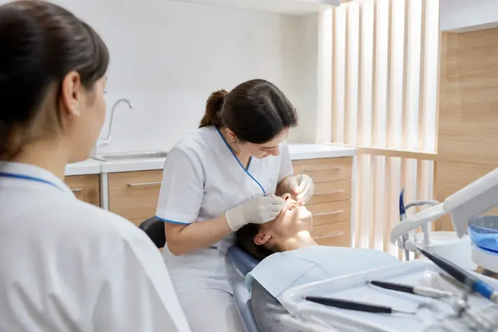 Chairside appointment: dentist at work, over-the-shoulder view of the assistant — illustration for the section "Flap surgery with recession coverage"