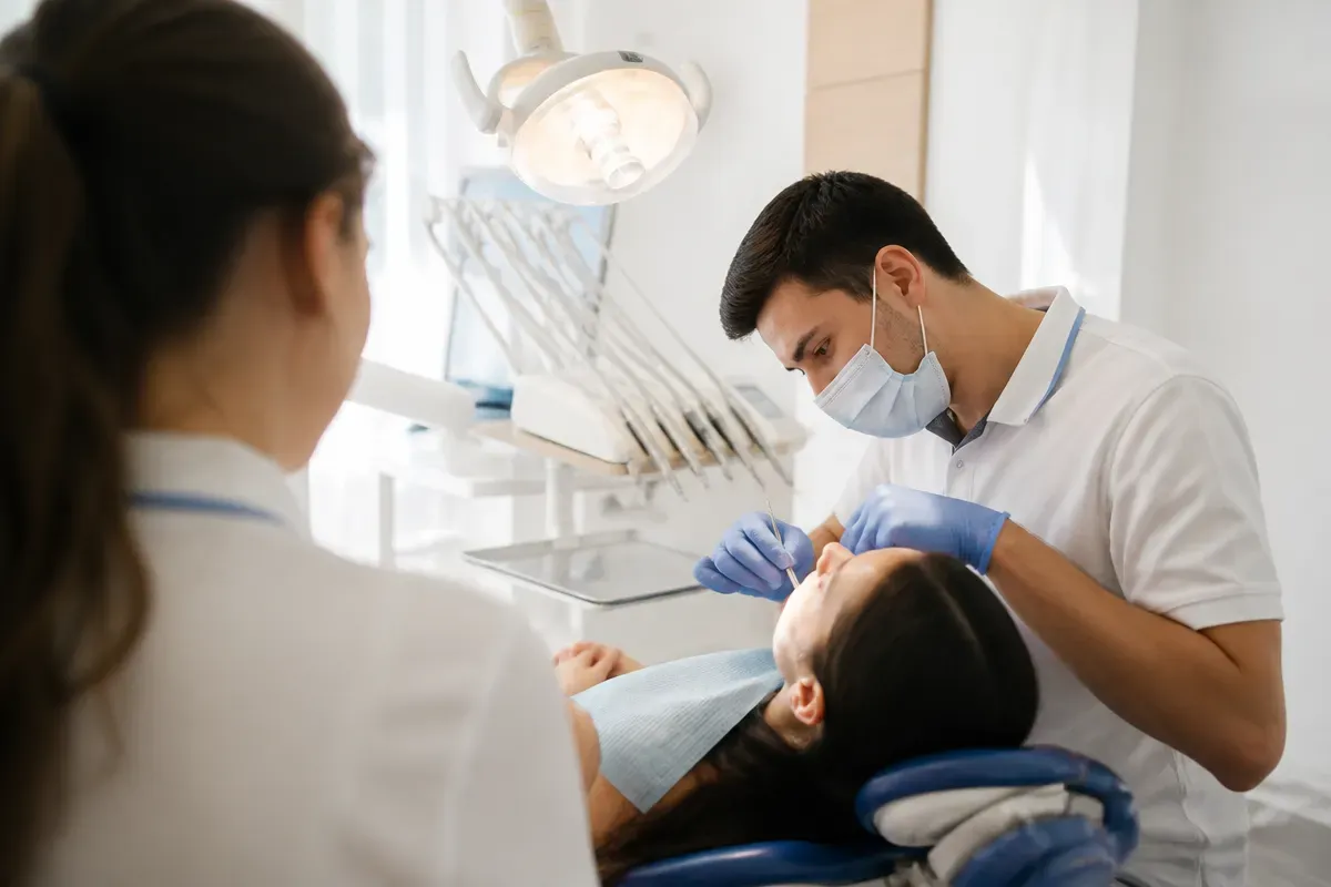 Chairside visit: dentist at work, over-the-shoulder shot past the assistant — illustration for the section "Which medications are effective for stomatitis"