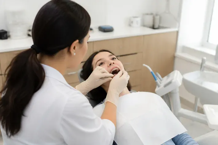 Chairside visit: dentist at work, over-the-shoulder shot of the assistant — illustration for the section "How the Damon Q self-ligating system works: mechanism, archwires, activations"