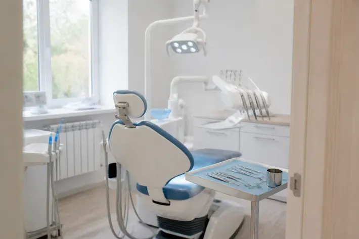 Treatment room prepared for an appointment: dental chair, lamp, and tray of instruments — illustration for the section "Metal-ceramic crown as a component of a dental bridge"