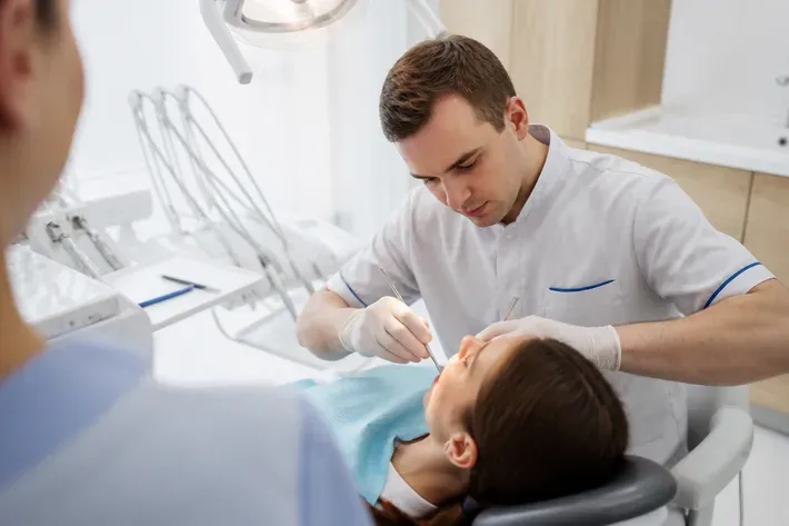 Орындық жанындағы қабылдау: жұмыс үстіндегі дәрігер, көмекшінің иығынан түсірілген сурет — «Силикон» бөліміне иллюстрация
