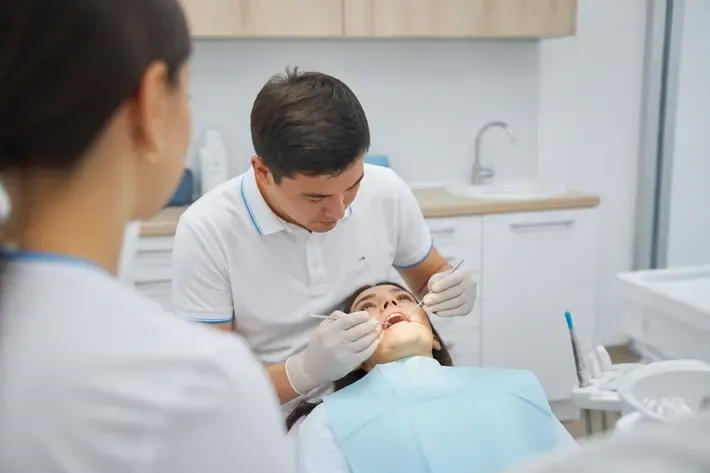 Chairside appointment: dentist at work, over-the-shoulder view of the assistant — illustration for the section "Restoration with and without a post"