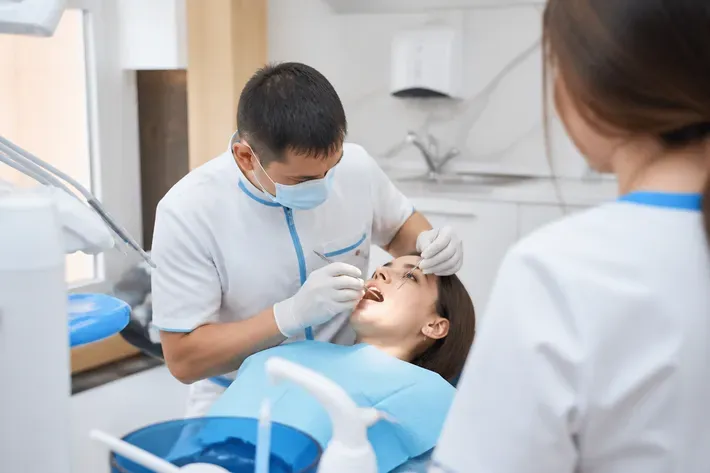Chairside appointment: dentist at work, over-the-shoulder shot of the assistant — illustration for the section "What materials are used for prosthetics"
