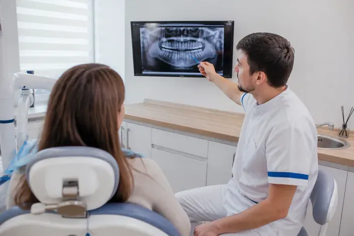 The doctor shows the patient the scan on the screen and explains the treatment plan — an illustration for the section "Complications after prosthetics"