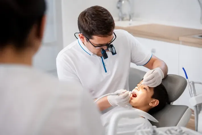 Chairside appointment: dentist at work, over-the-shoulder shot of the assistant — illustration for the section "What materials are used for restoring children's teeth"