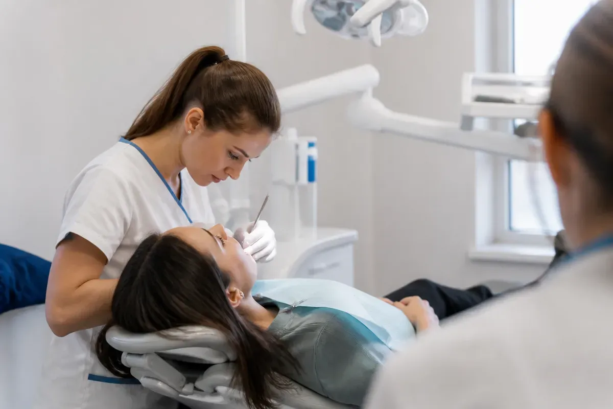 Chairside appointment: dentist at work, shot over the assistant's shoulder — illustration for the section "Metal braces: features"