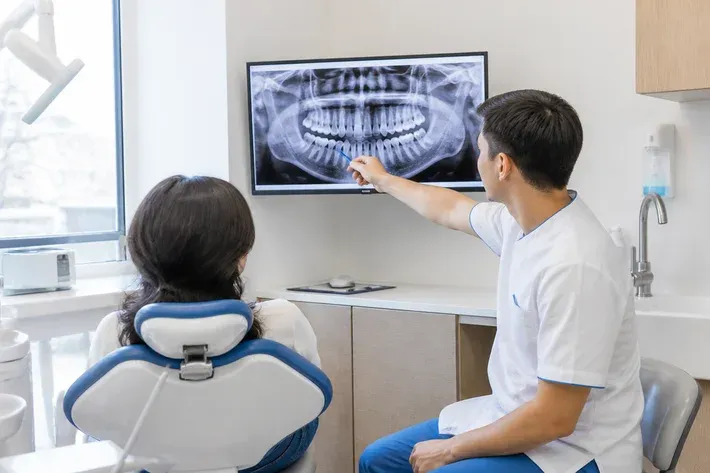 Doctor showing the patient an image on screen and explaining the treatment plan — illustration for the section "Damage to adjacent structures"