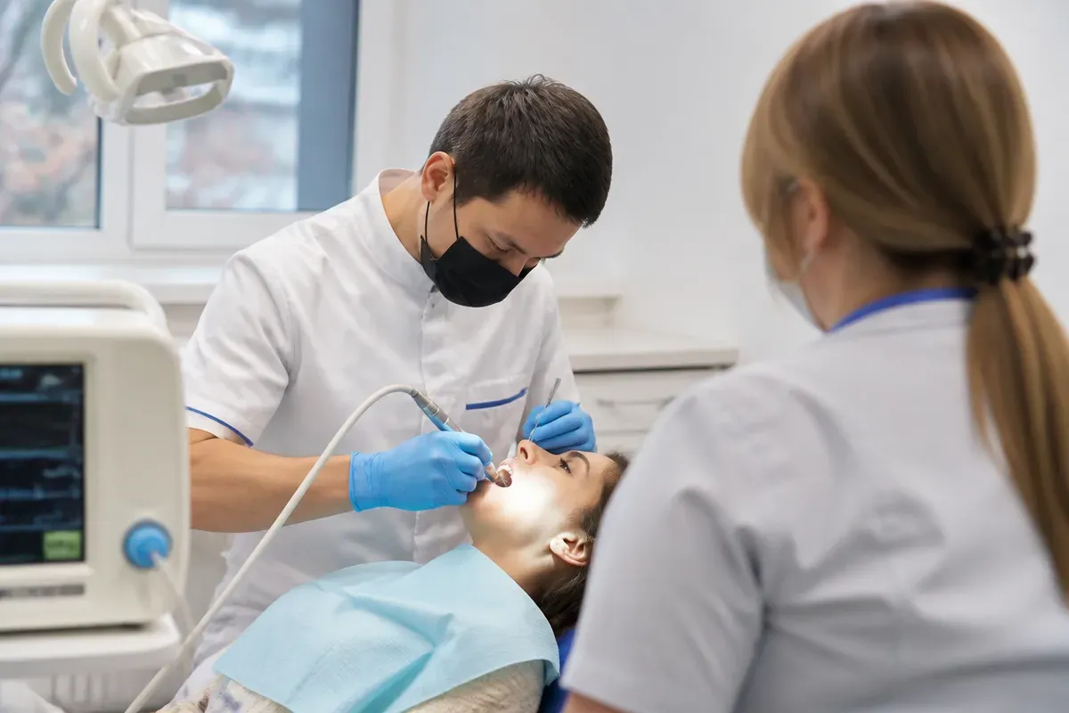 Креслодағы қабылдау: жұмыс үстіндегі дәрігер, ассистенттің иығынан түсірілген сурет — «Процедура кезіндегі жағдайды бақылау» бөліміне иллюстрация