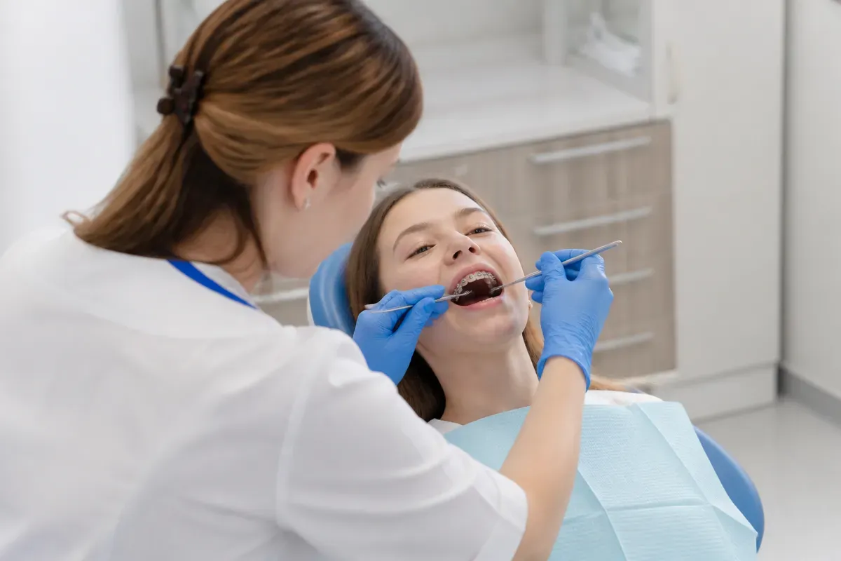 Chairside appointment: dentist at work, over-the-shoulder shot of the assistant — illustration for the section "Ceramic self-ligating braces"
