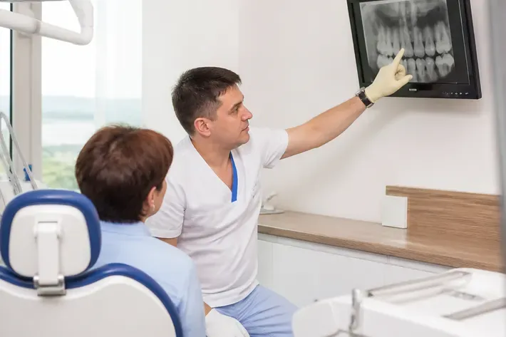 Doctor showing the patient an image on the screen and explaining the treatment plan — illustration for the "Root amputation" section
